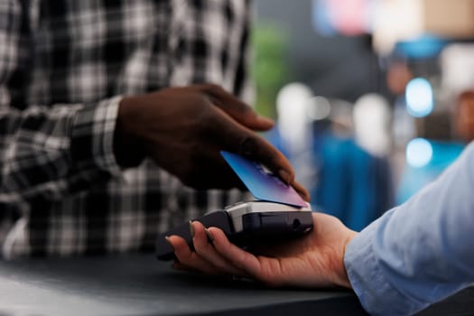 African american man shopper putting credit card on pos terminal paying formal for wear at counter desk in modern boutique, buying stylish clothes, fashionable accessories. Fashion concept. Close up