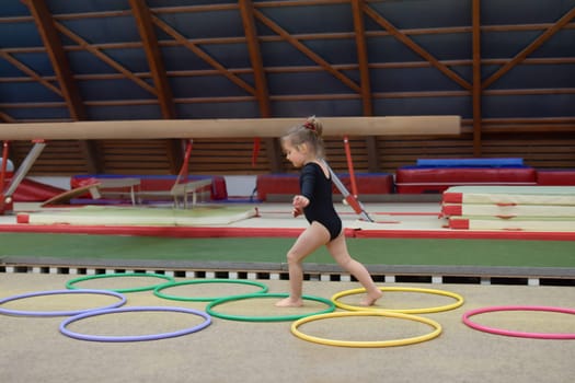 A three-year-old girl runs through hula hoops in the gym