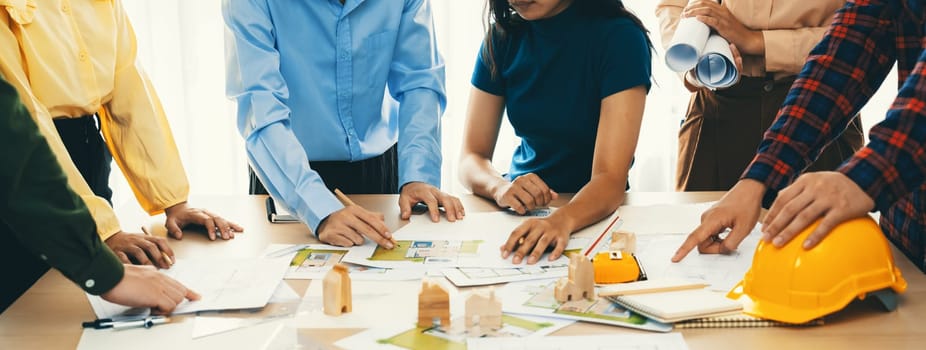 Professional architect engineer team discussion about architectural project on meeting table with wooden block and blueprint scatter around. Design and cooperate concept. Closeup. Delineation.