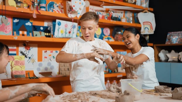 Diversity happy student playing clay while put on shirt at art lesson. Multicultural highschool children working and cup of clay at pottery workshop. Creative activity concept. Education. Edification.