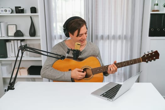 Host channel in smart singer with smiling face, playing guitar along singing, broadcasting on social media channel, wearing headphones to record video streamer at modern studio recording. Pecuniary.