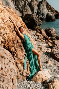 Woman green dress sea. Woman in a long mint dress posing on a beach with rocks on sunny day. Girl on the nature on blue sky background