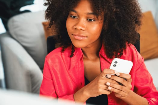 Young African businesswoman focusing information on smartphone and researching information data center on website pc and smartphone. Theme of place work in comfy room with plain color. Tastemaker.