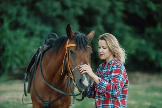 Happy blonde with horse in forest. Woman and a horse walking through the field during the day. Dressed in a plaid shirt and black leggings