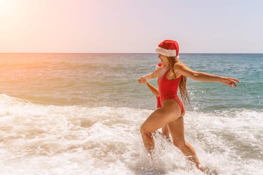 Women in Santa Claus hats run into the sea dressed in red swimsuits. Celebrating the New Year in a hot country.