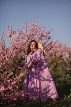 Woman blooming peach orchard. Against the backdrop of a picturesque peach orchard, a woman in a long pink dress and hat enjoys a peaceful walk in the park, surrounded by the beauty of nature