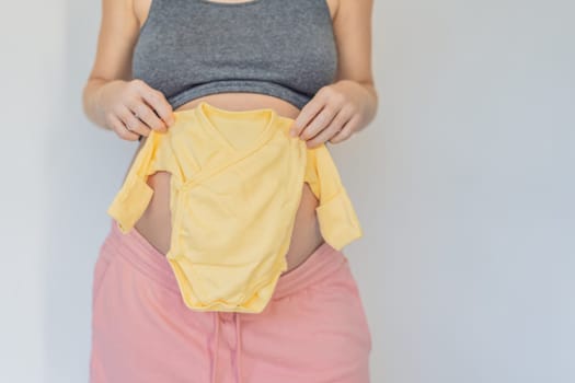 In a tender moment of anticipation, a pregnant woman cradles her unborn baby's clothes in her hands, savoring the sweetness of preparing for the little one's arrival.