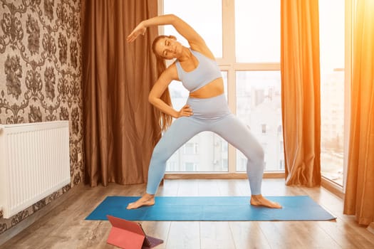 Young athletic attractive woman practicing yoga doing exercises. Works out at home or in a yoga studio, sportswear, blue pants and a full-length top indoors. Healthy lifestyle concept.