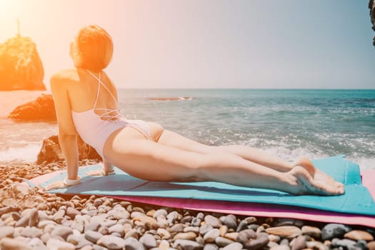 Young woman with black hair, fitness instructor in pink sports leggings and tops, doing pilates on yoga mat with magic pilates ring by the sea on the beach. Female fitness daily yoga concept