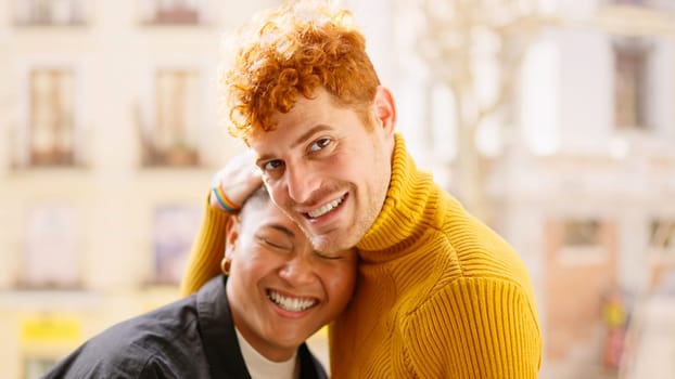 Gay couple in a tender scene smiling at camera in the balcony at home