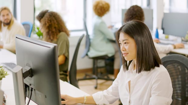 Asian woman working happily in a coworking space with other colleagues
