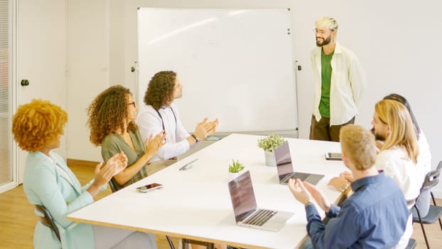 Diverse coworkers applauding a man after a presentation using white board in a meeting room