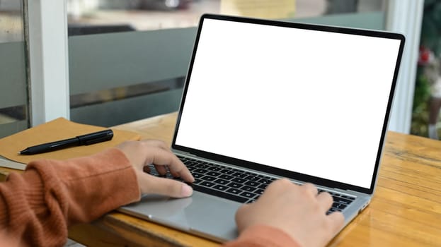 Cropped shot young woman typing on laptop keyboard with white empty screen for advertising.