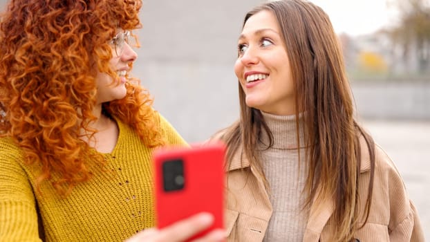 Two female friends surprised while using phone together in the street