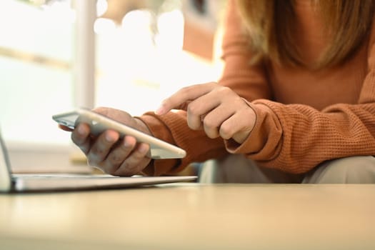 Young woman holding mobile phone and typing message while sitting in coffee shop.