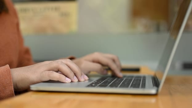 Side view of woman hands typing on laptop while working remotely in coffeeshop.