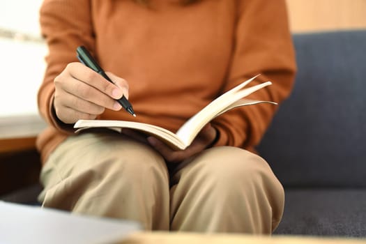 Unrecognizable young woman writing notes in personal daily planner or planning workday.