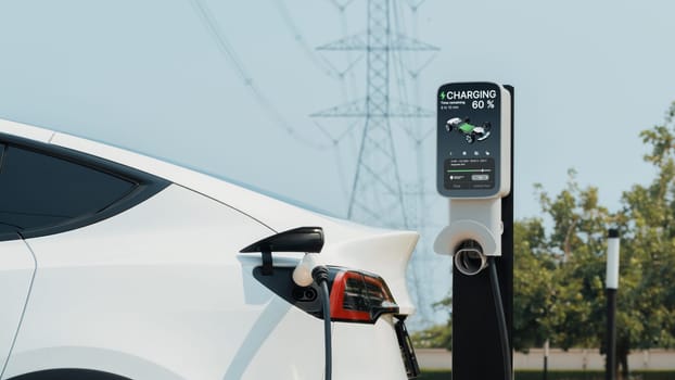 Electric vehicle or EV car recharge battery at charging station connected to power grid tower electrical industrial facility as electrical industry for eco friendly vehicle utilization. Expedient