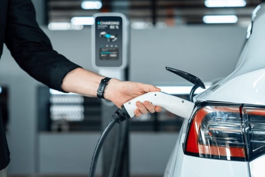 Young man travel with EV electric car to shopping center parking lot charging in downtown city showing urban sustainability lifestyle by green clean rechargeable energy of electric vehicle innards