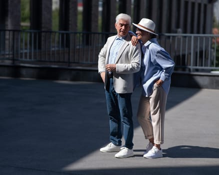Stylish mature couple. Gray-haired man and woman holding hands while walking around the city