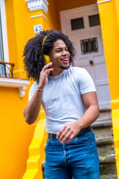 Vertical photo of an african young man listening to music with headphones in the street next to yellow house