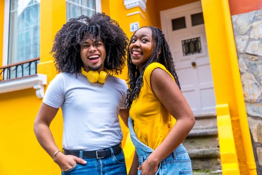 Portrait of a happy urban african couple smiling outdoors next to a house with yellow facade