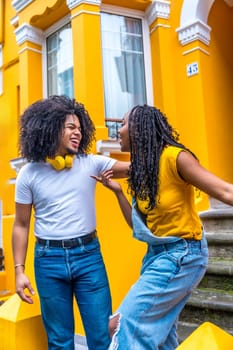 Happy african couple with headphones chilling next to a house with yellow facade