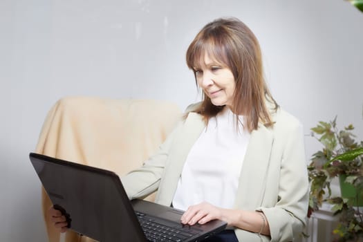 Elderly lady with a laptop in the room. A businesswoman is a leader, a manager is working. Grandma communicates with her grandchildren on the Internet