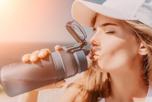 Fintess woman drinking water. Happy, active middle aged woman standing on beach and drinking water after excersise. Concept of lifestyle, sport. Close up.