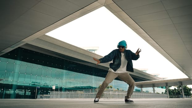 Motion shot of happy hipster practice b boy dance with stylish cloth at building. Dancer enjoy show footstep performance. Modern lifestyle, break dancing. Slow motion. Outdoor sport 2024. Sprightly.