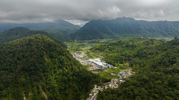 Aerial drone of small town among the mountains with jungle and rainforest. Berastagi, Sumatra. Indonesia.