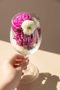 Female hand holding Wine glass full of colorful flowers. Creative concept for holidays greeting card postcard. Minimalistic isometric style. Drinking beauty bouquet. Copy space