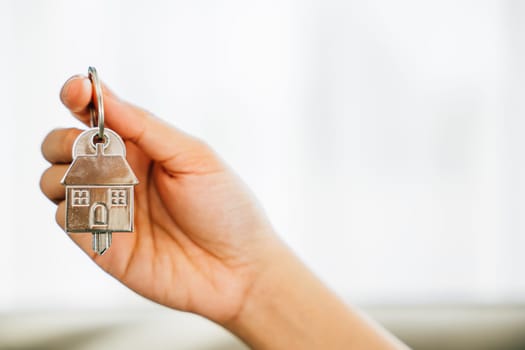 Woman's hand holds house key showcasing homeowners' achievement. Agent displays model home signifying real estate success. Confidence and happiness resonate.