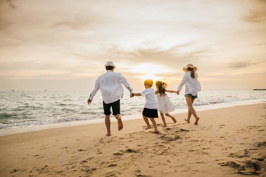 Back of happy Asian parents with their daughters enjoying playful at beach. Little girls bond with their mother and father running jumping and pretending to fly with arms wide open. Family fun in sun.