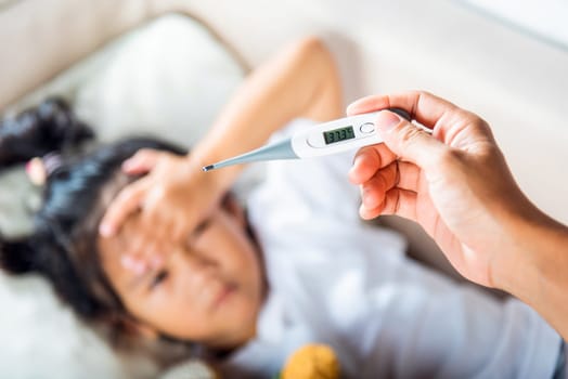 Sick kid. Mother parent checking temperature of her sick daughter with digital thermometer in mouth, child laying in bed taking measuring her temperature for fever and illness, healthcare