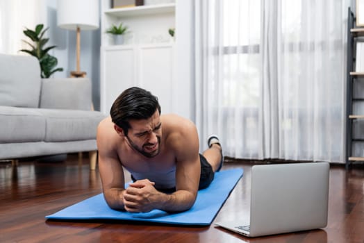 Athletic and sporty man suffer from exercise injury during online body workout exercise session at home. Painful ache from injured muscle accident during gaiety home exercise workout training concept.