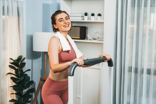 Athletic and sporty woman running on treadmill running machine during home body workout exercise session for fit physique and healthy sport lifestyle at home. Gaiety home exercise workout training.