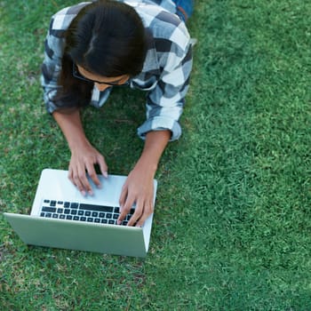 Above, grass and person typing on laptop in park with college research, project or learning on campus. University, student and girl reading online with ebook, education and study on lawn in garden.