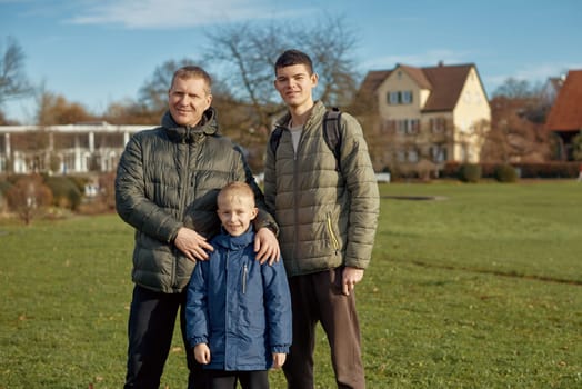 Family Harmony: Father, 40 Years Old, and Two Sons - Beautiful 8-Year-Old Boy and 17-Year-Old Young Man, Standing on the Lawn in a Park with Vintage Half-Timbered Buildings, Bietigheim-Bissingen, Germany, Autumn. Embrace the essence of family togetherness with this heartwarming image featuring a father, 40 years old, and his two sons - a beautiful 8-year-old boy and a 17-year-old young man. Standing on the lush lawn in a park with vintage half-timbered buildings in Bietigheim-Bissingen, Germany, this captures the warmth of familial bonds amidst the autumnal beauty.