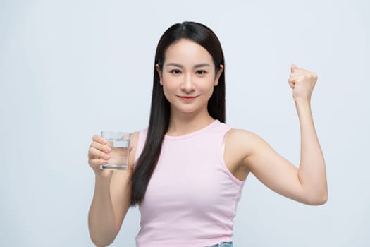 Smiling young Asian woman holding glass of fresh clean water  with raised arm on white