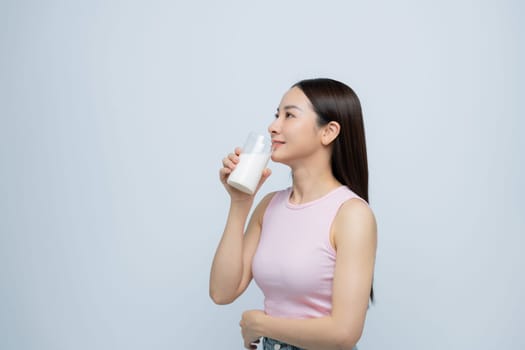A satisfied young asian woman drinking milk from the glass isolated over white background