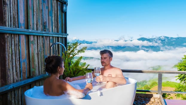 a couple of men and women in a bathtub looking out over the mountains of Chiang Rai Northern Thailand during vacation. Outdoor bathroom, young couple in a bath tub