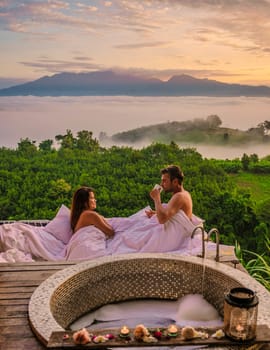 a couple of men and women in a bathtub looking out over the mountains of Northern Thailand during vacation. Outdoor bathroom, and bathtub during sunset at the mountains with mist and fog