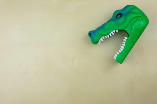 Plastic green dinosaur head with open mouth and sharp teeth on the table, child favorite toy
