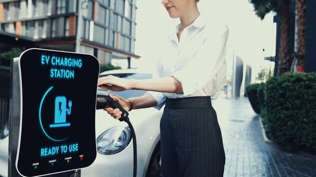 Businesswoman recharge her electric car from charging station at city center or public parking car. Eco friendly rechargeable car using alternative clean energy. Peruse