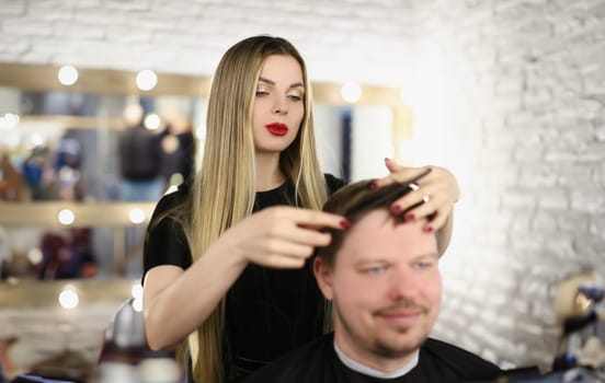 Stylish girl hairdresser combing hair to a man, close-up. Woman master makes a haircut to a guy, fashion