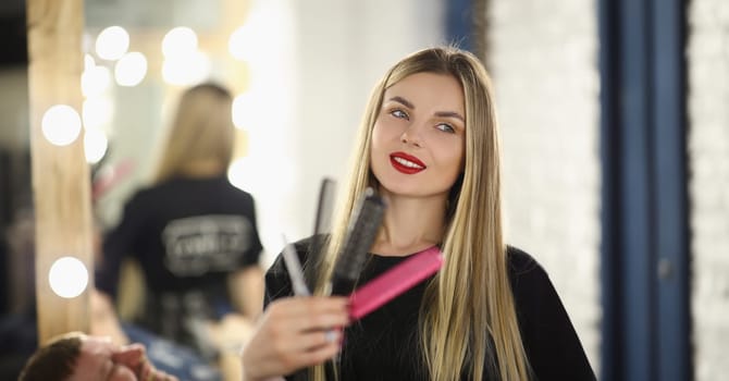 Happy young girl hairdresser holding different combs, close-up. Beauty salon stylist woman, profession