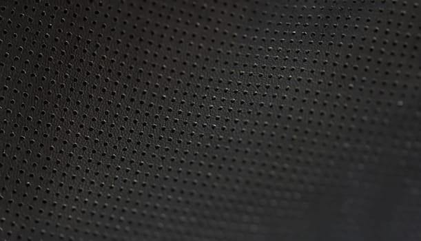 Black leather fabric pattern of small holes, close-up. Perforated matte texture. A macro shot of dark background