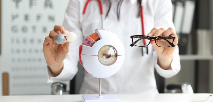 In female hands glasses for vision are next to the model of the eye, close-up. Protection of lenses from ultraviolet radiation
