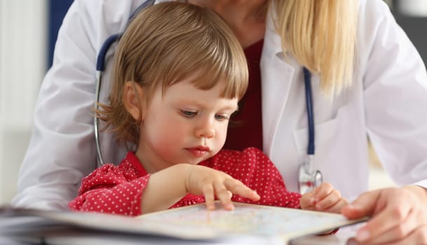 Female pediatrician next to a little girl in a red dress, close-up. Doctor's consultation, intelligence test